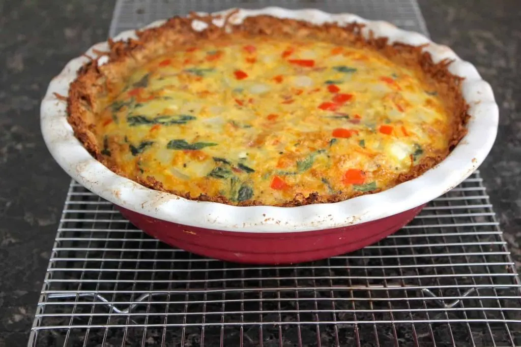 Baked ham and spinach quiche in a red ceramic pie plate.