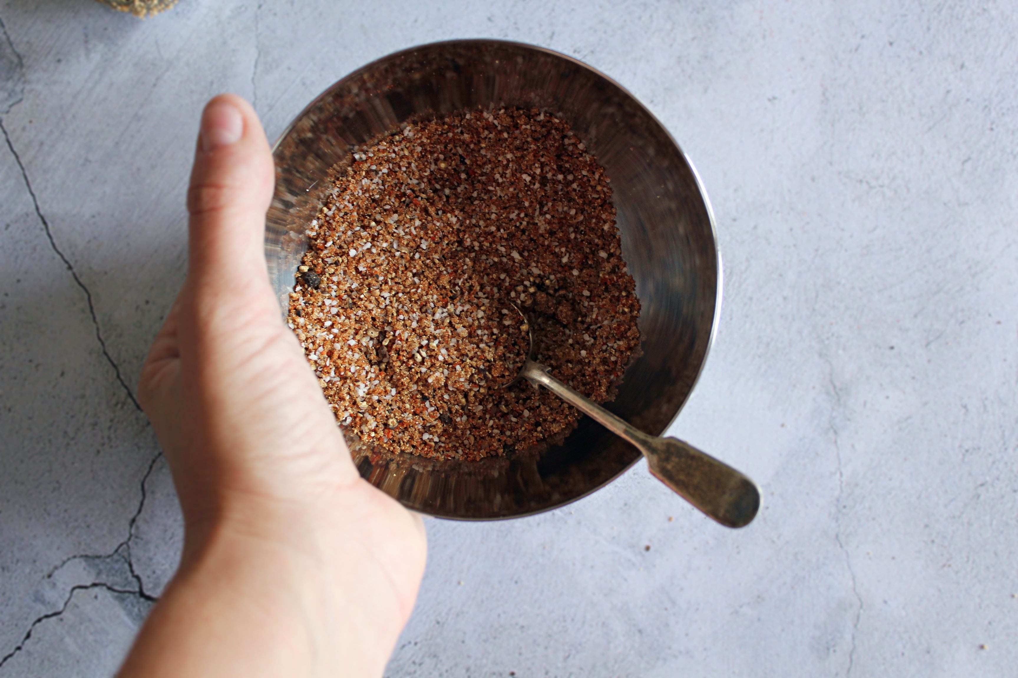 A hand holding a stainless steel bowl containing the pork rub.
