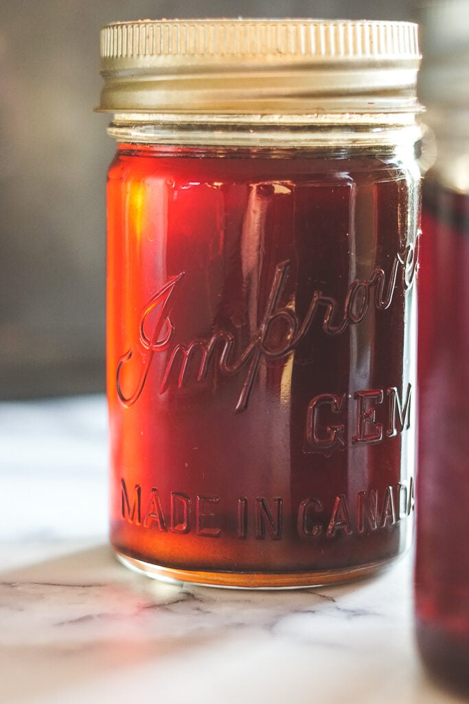 A mason jar with rich, deep brown homemade kahlua being back lit by the sun. 