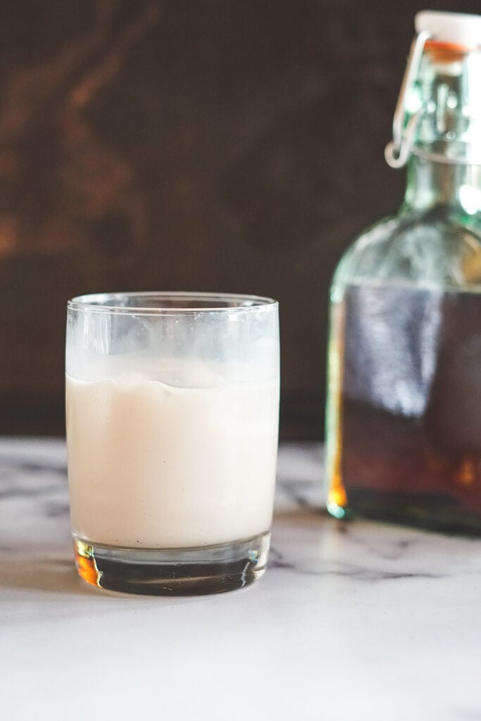 A stirred White RUssian cocktail in a short glass, with a jar of homemade kahlua in the background.