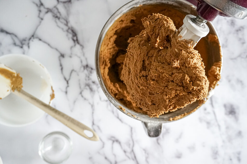 A tilt head mixer propped open with rich brown ginger snap cookie batter all over the mixing paddle.