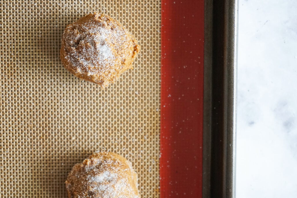 Unbaked ginger snap cookie dough balls with white granulated sugar sprinkled on top.