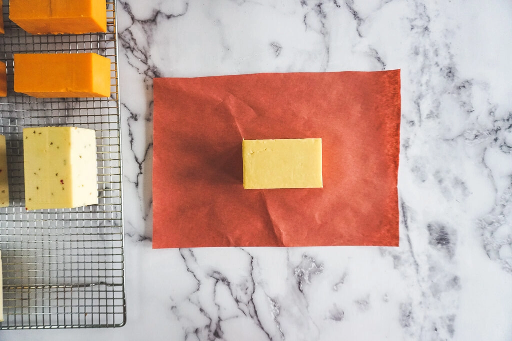 A white block of smoked old cheddar cheese sitting on a piece of peach butchers paper.