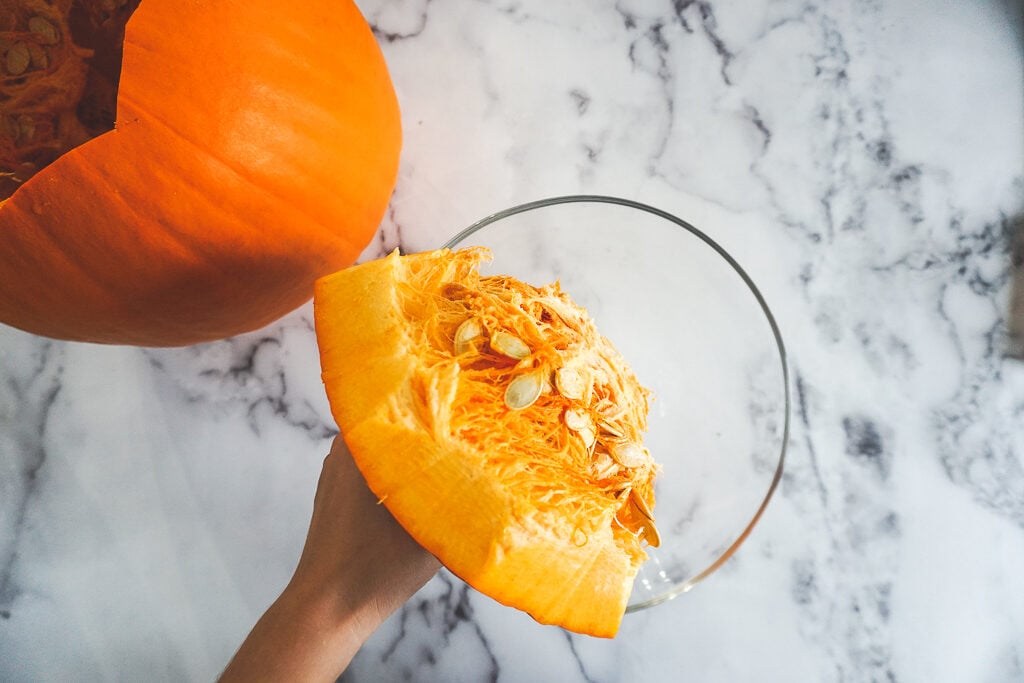 Holding the top of a pumpkin while the seeds and stringy guts dangle over a glass bowl.