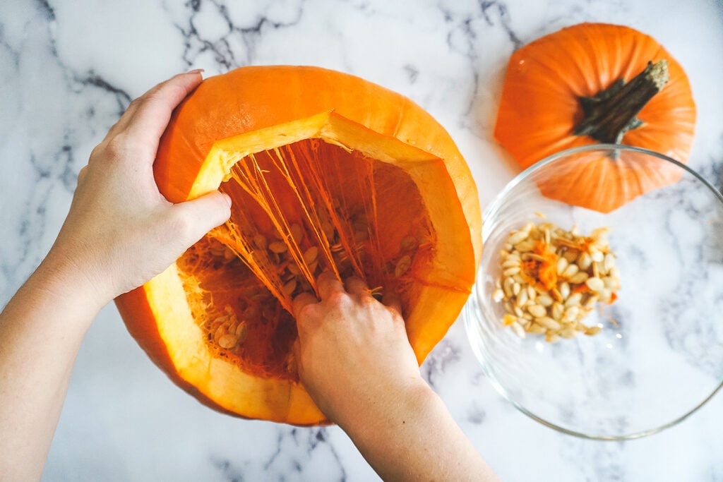 A hand pulling down through the stinggy orange innards of a pumpkin.