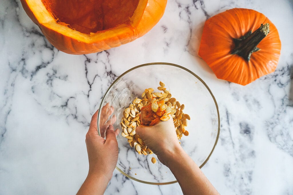 A hand squeezing pumpkin pulp to extract the seeds for roasting.