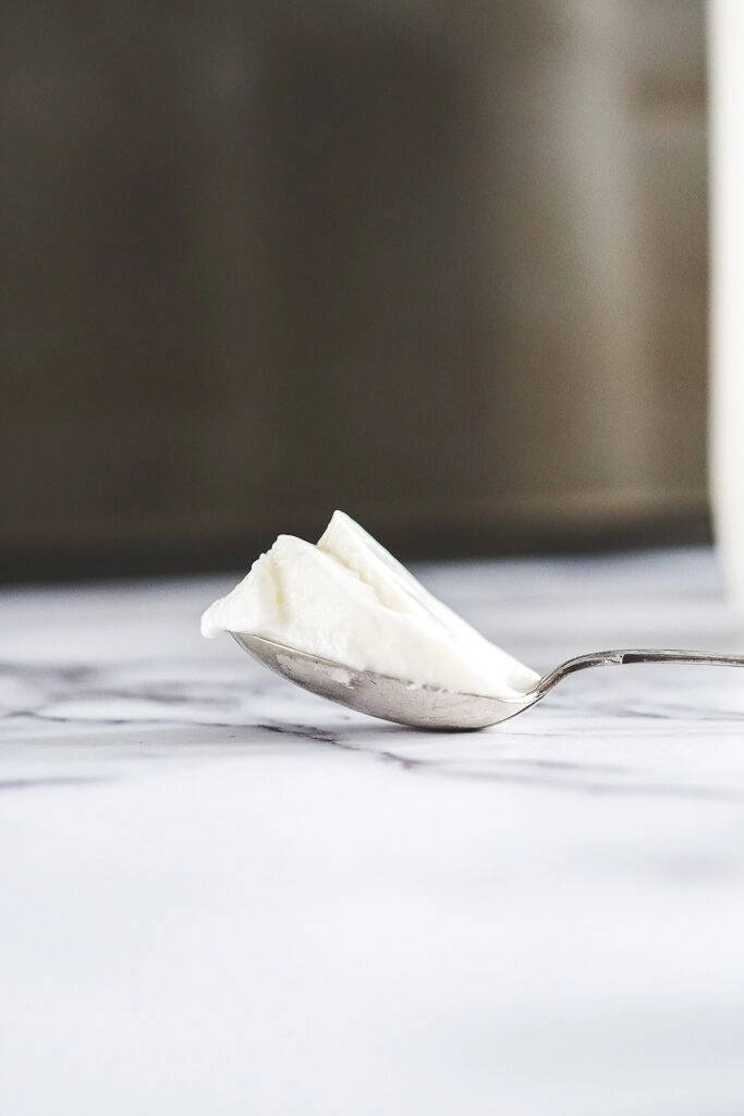 A spoon with thick sous vide yogurt showing the texture.