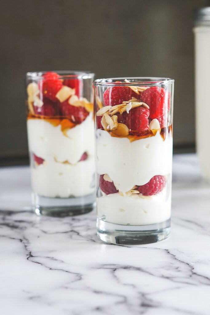 A sous vide yogurt parfait with layered yogurt, raspberries, sliced almonds and maple syrup drizzle.