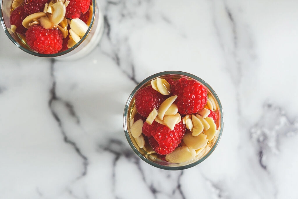 Overhead view of sous vide yogurt in a slender cup - topped with raspberries and slivered almonds.