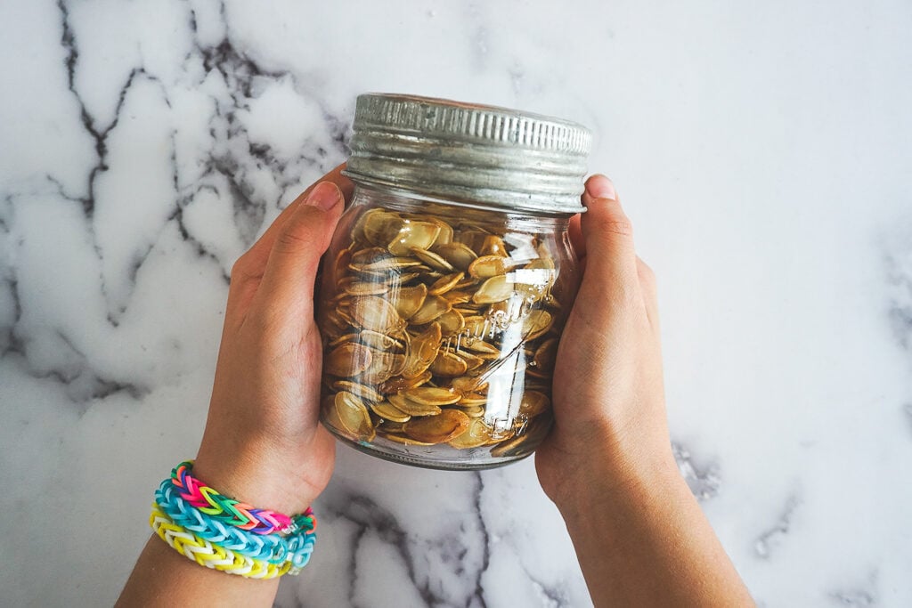 A child's hands holding a mason jar filled with smoked pumpkin seeds.