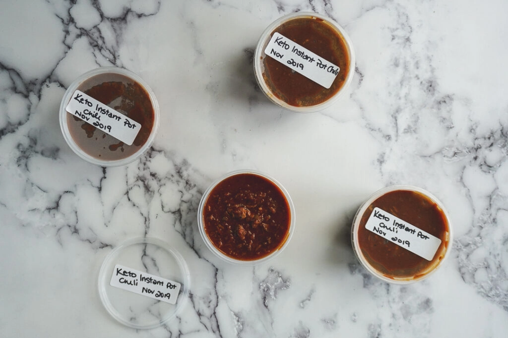Cooked chili placed in restaurant style prep containers with white labels, and the words Keto Instant Pot Chili Nov 2019 scrawled on top.