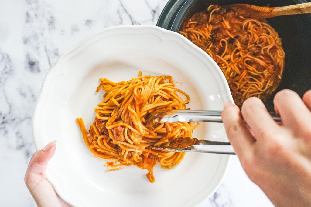 Using tongs to serve spaghetti into a white bowl. 