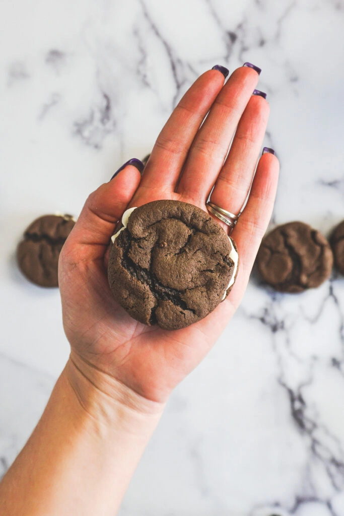 A hand with long purple finger nails holding a homemade oreo.