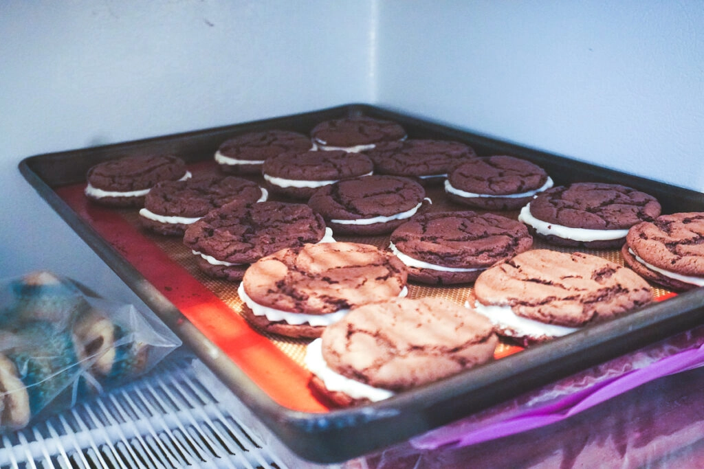 Homemade oreo cookies line up on a baking sheet in the freezer.