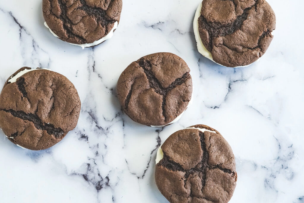 Crackled tops of homemade oreos with white cream cheese frosting peeking out.