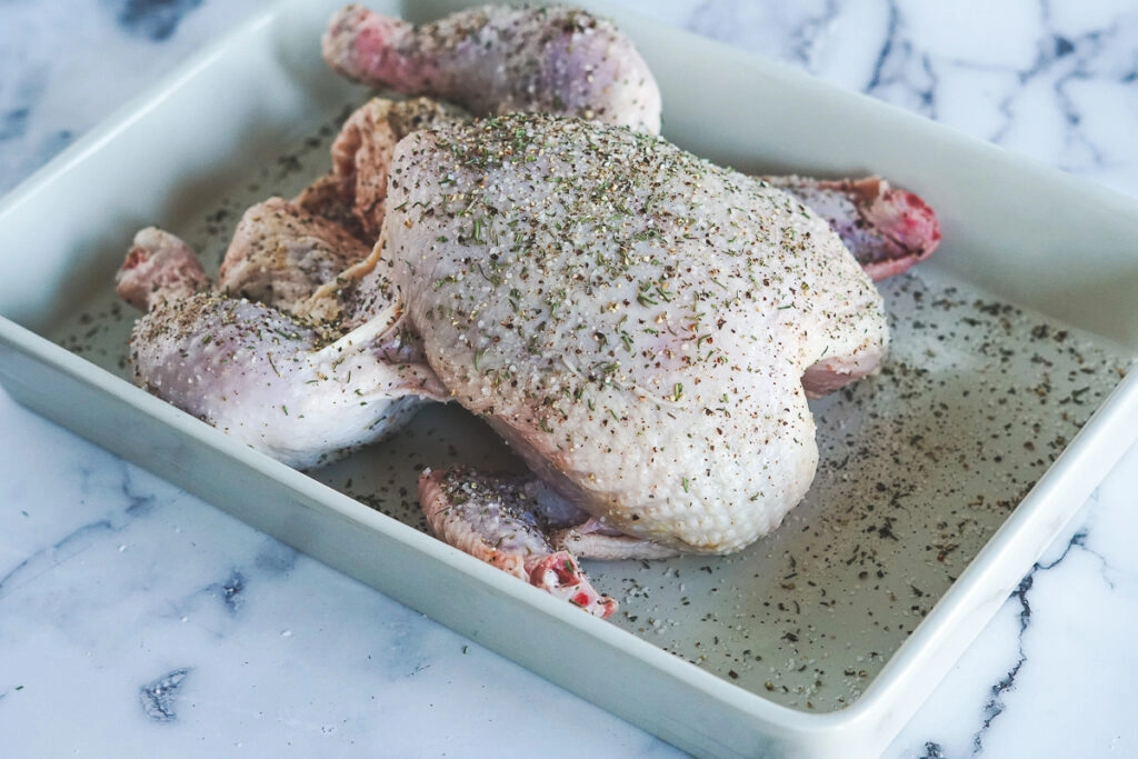 Untrussed chicken with herbs sprinkled on it.