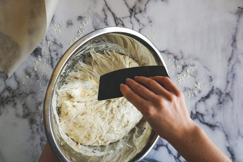 Using a bowl scraper to turn the dough onto the counter. 