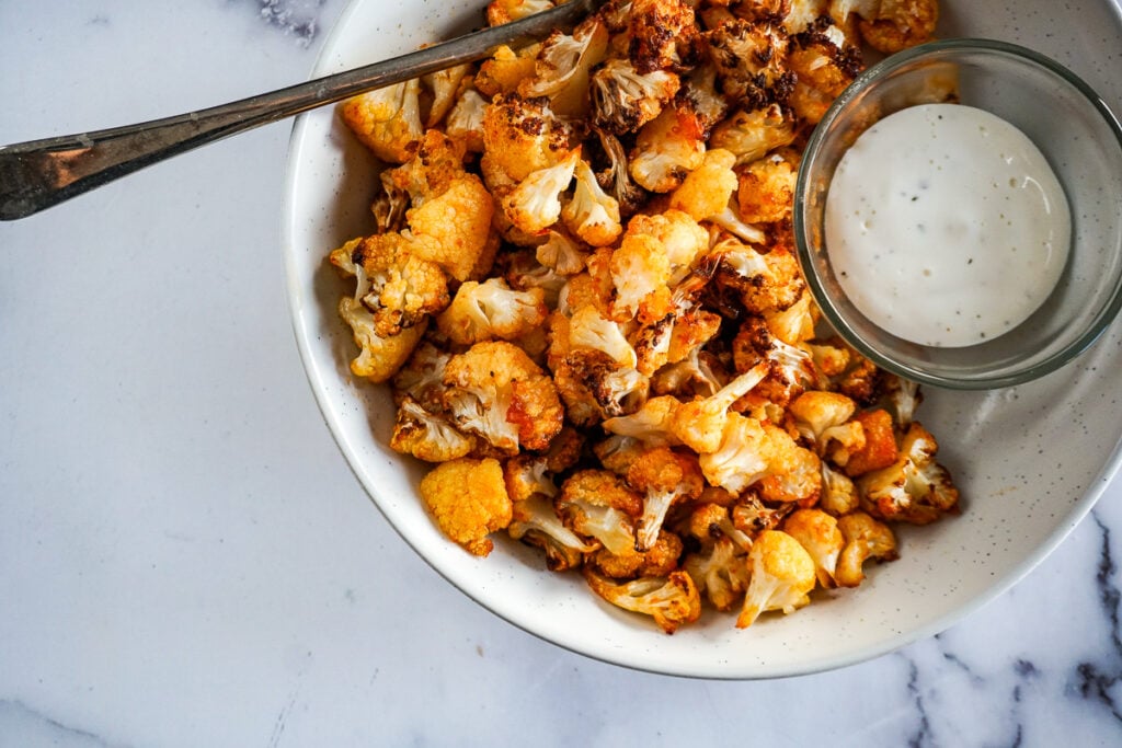 A bowl filled with sriracha maple air fried cauliflower with a spoon in it.