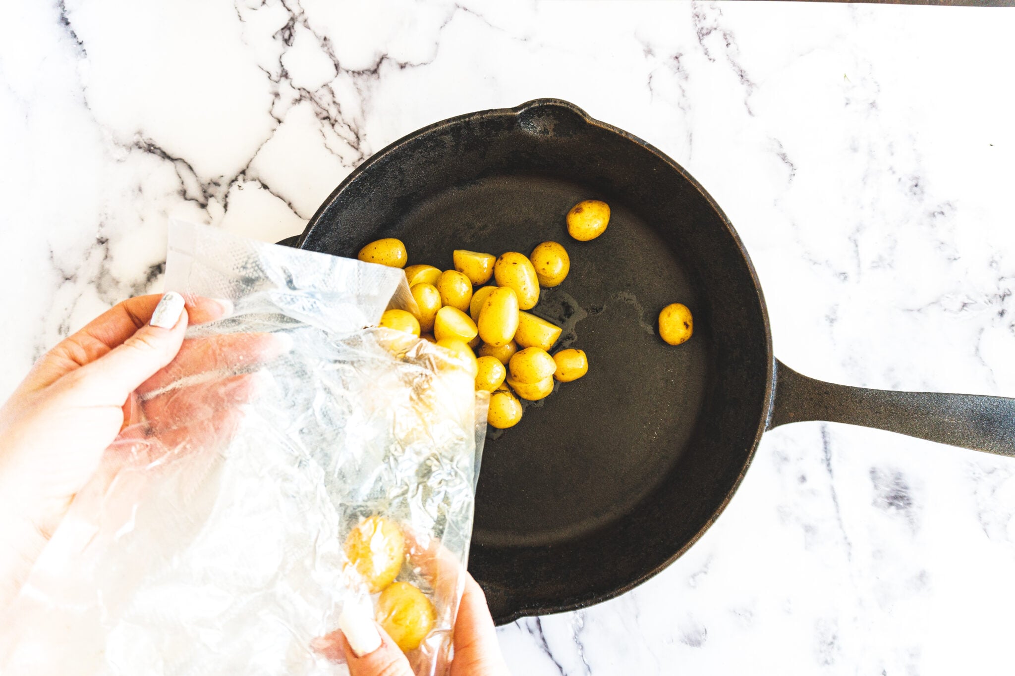 Cooked sous vide potatoes being poured from the bag into a heated cast iron skillet.