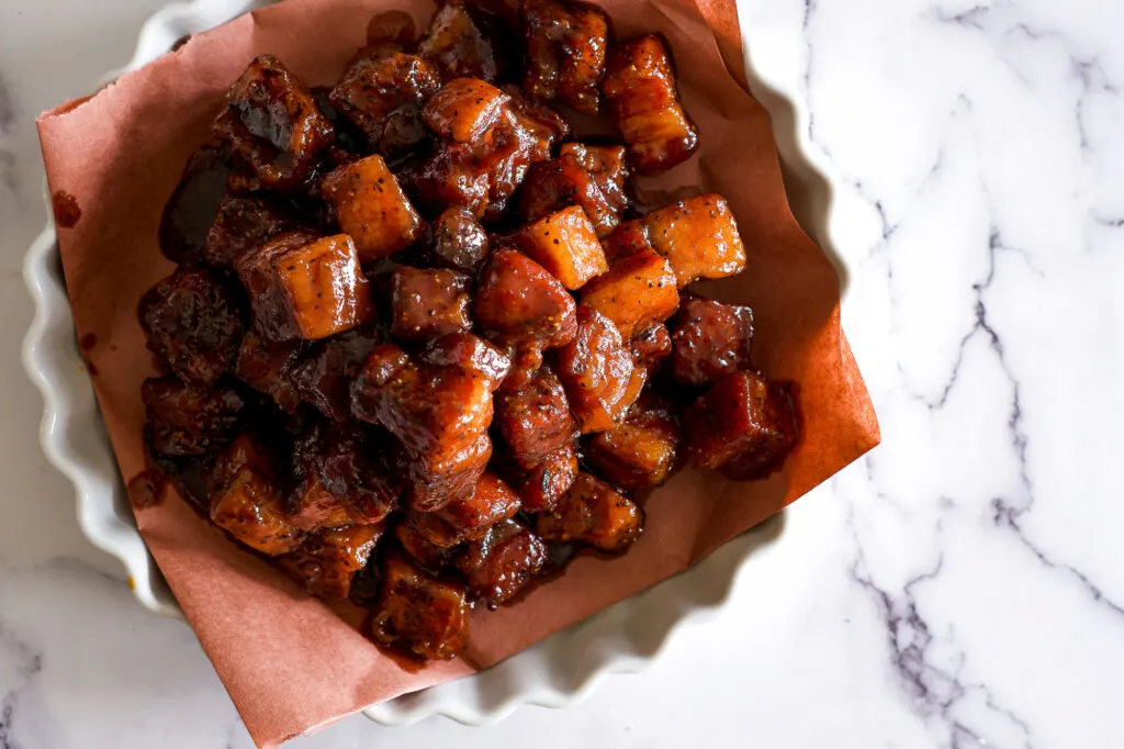 A pile of saucy pork belly burnt ends in a white dish.