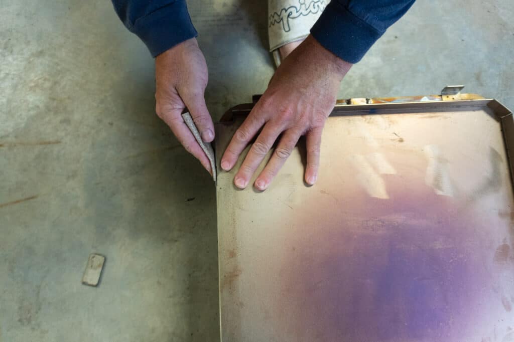 Mans's hands sanding steel burrs with sand paper.