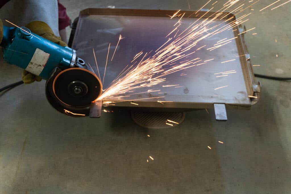 Angle grinder cutting off the front tabs of the Green Mountain pizza oven.