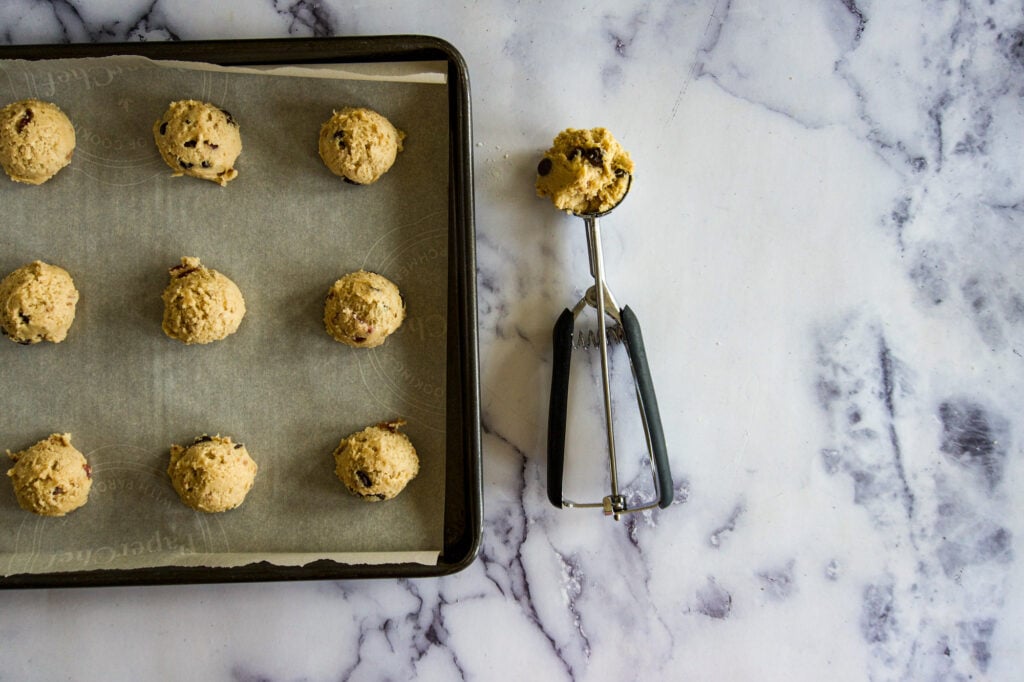 Bacon chocolate chip cookie dough balls on a cookie sheet with a cookie scooper.