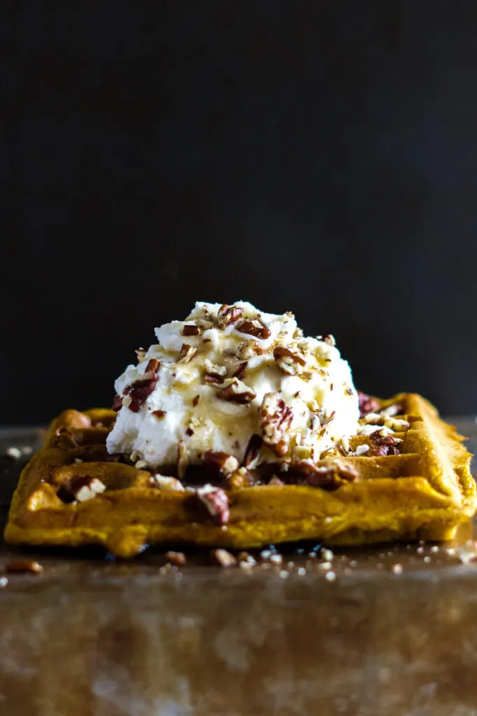 Pumpkin waffles topped with whipping cream crushed pecans and maple syrup.