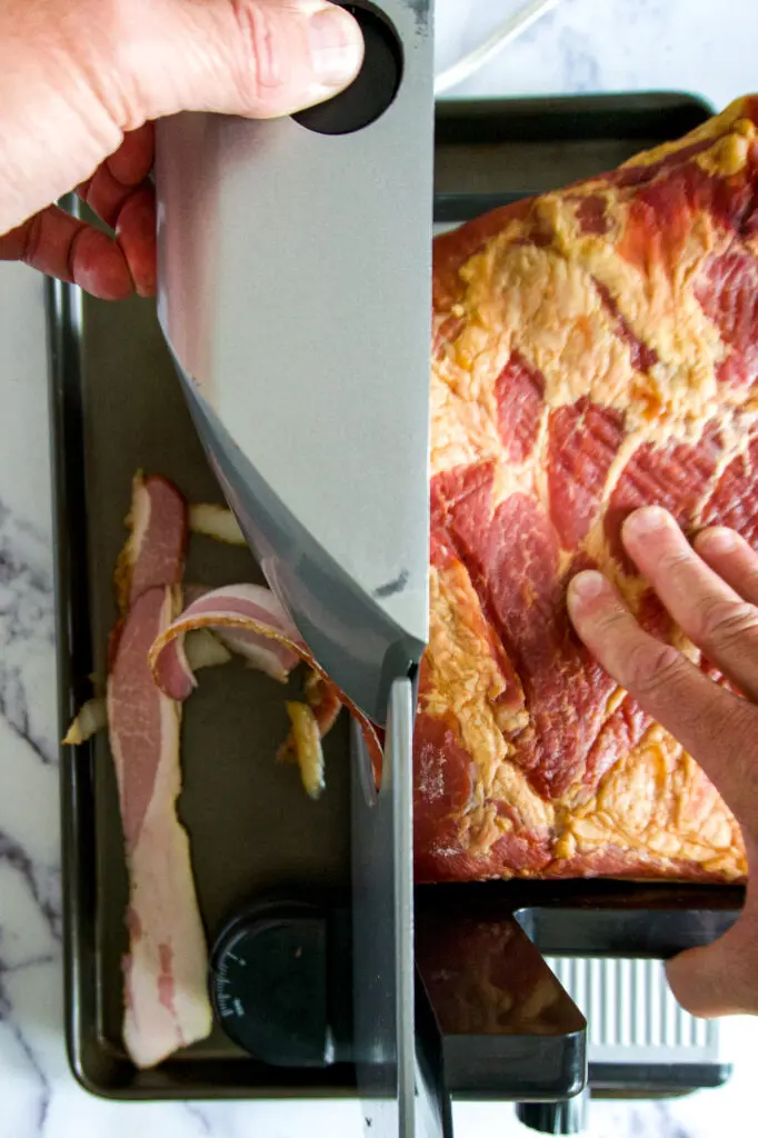 Using a meat slicer to slice smoked bacon.