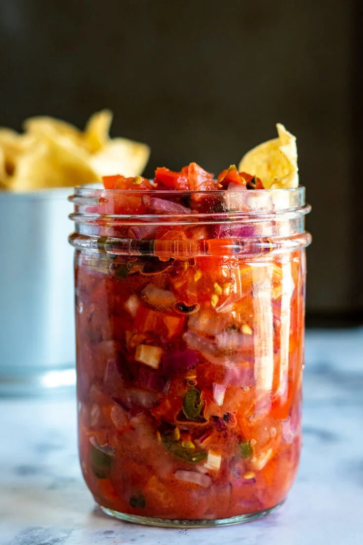 A jar of smoked salsa with a chip dipped in it.