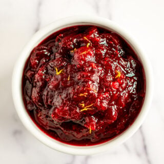 Homemade cranberry sauce topped with orange zest in a white bowl.