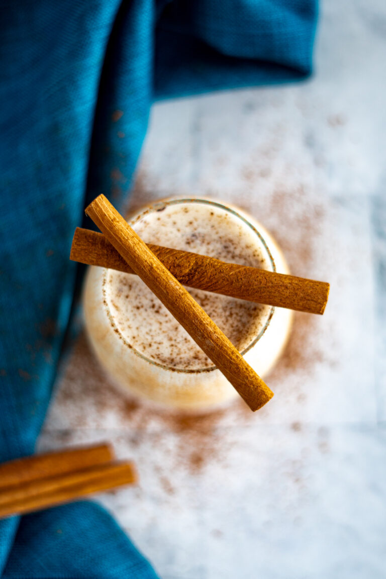 Overhead view of sous vide eggnog in a glass, garnished with ground nutmeg and two cinnamon sticks