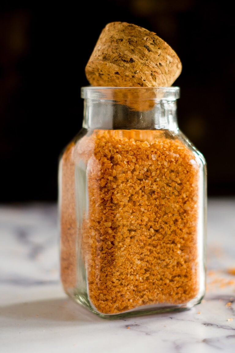 A glass jar with a cork lid filled with orange sriracha salt.