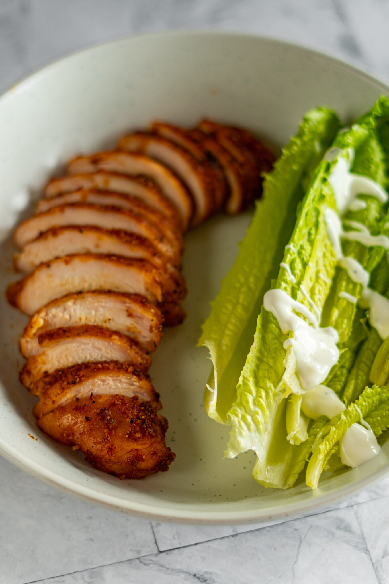 Sliced smoked chicken breast in a bowl with romaine salad.