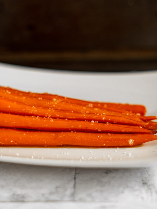 Sous vide carrots in a white dish with coarse salt sprinkled on them.