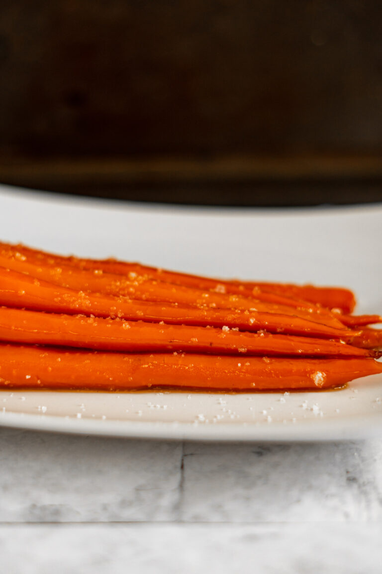 Sous vide carrots in a white dish with coarse salt sprinkled on them.