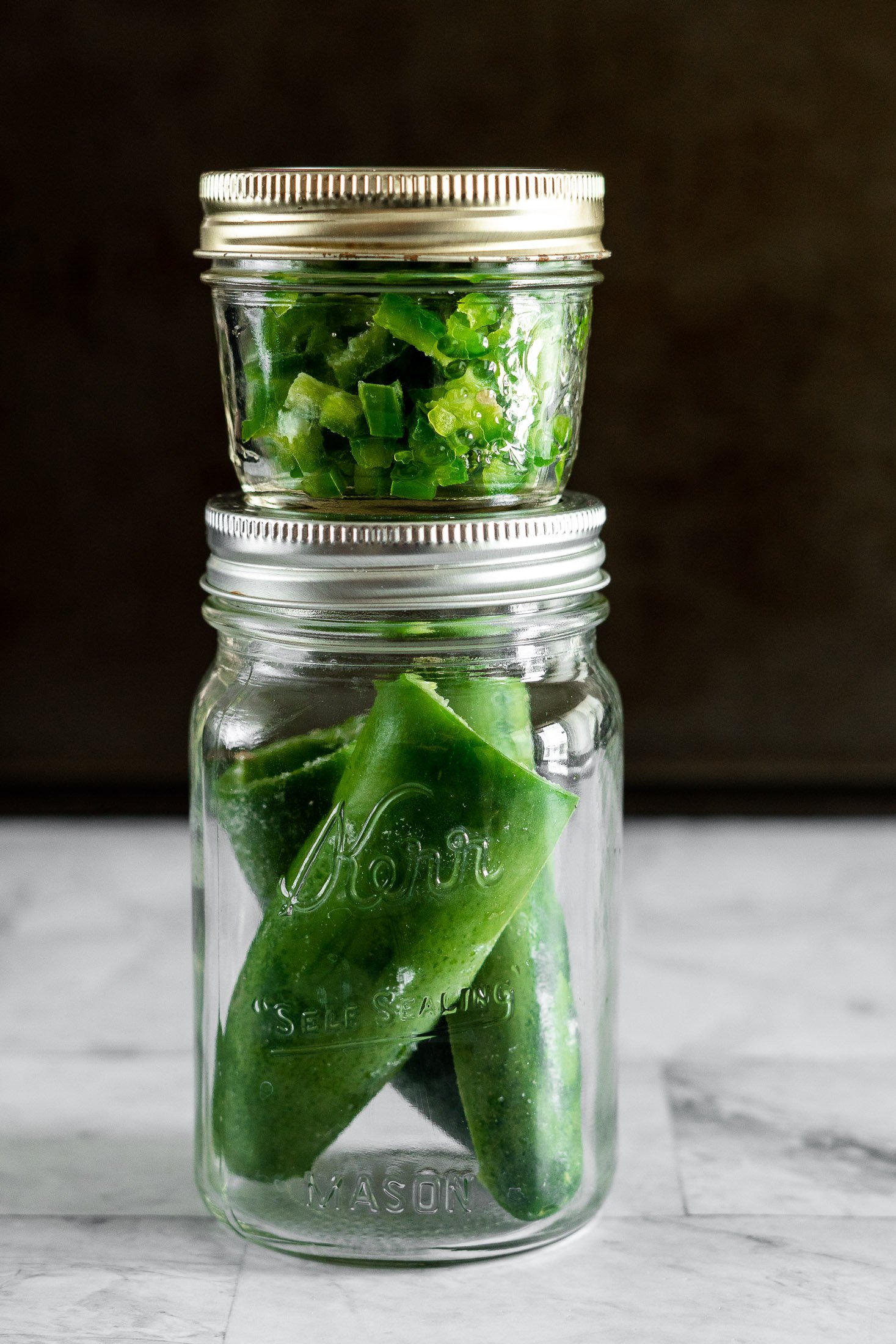 Two stacked jars filled with frozen jalapeno peppers. 