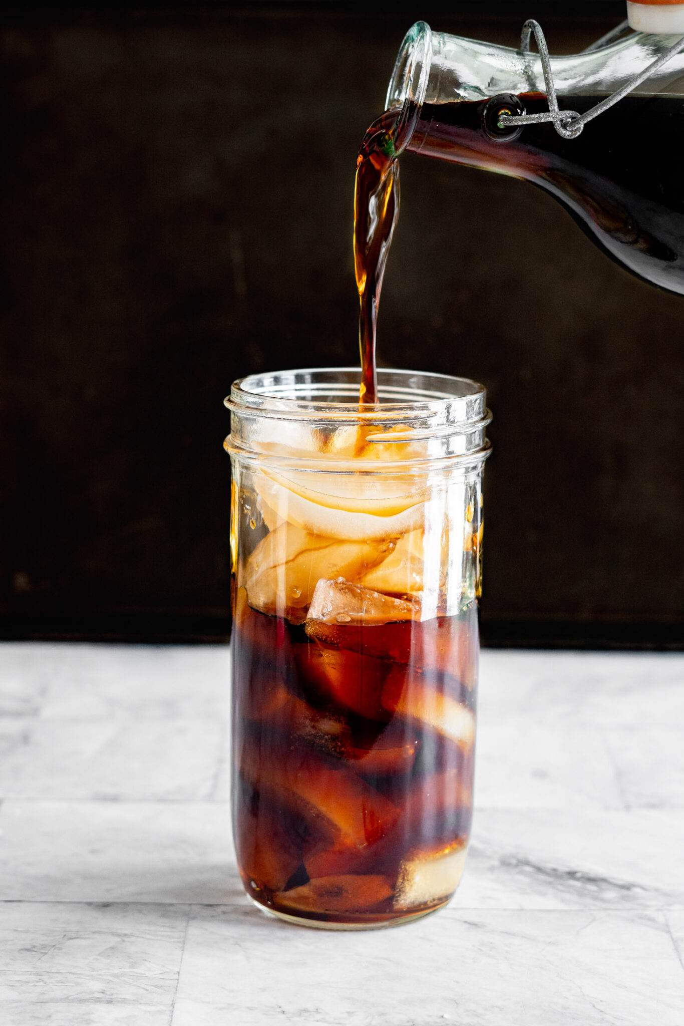 Pouring cold brew coffee into a large mason jar filled with ice.