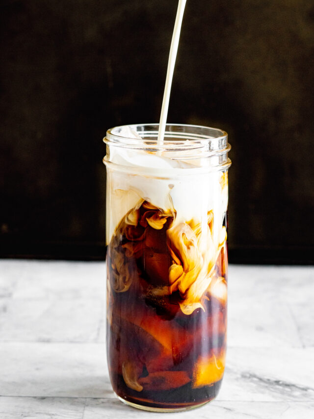 Pouring cream into a jar filled with cold brew sous vide coffee and ice