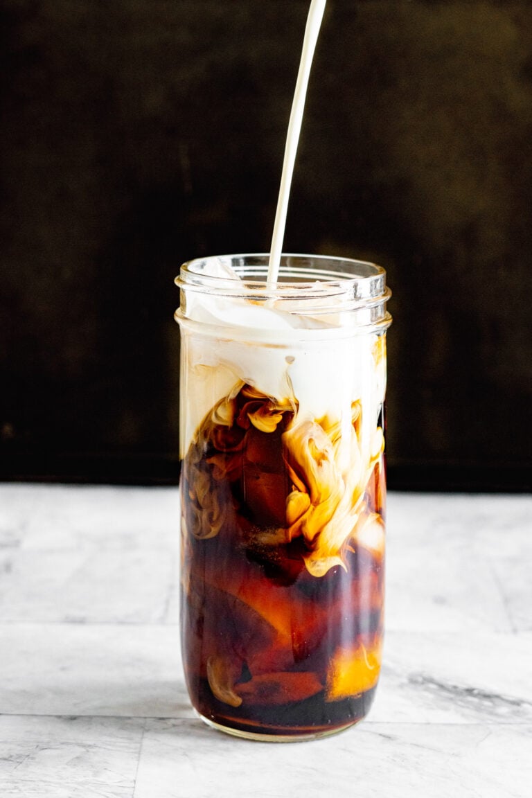 Pouring cream into a jar filled with cold brew sous vide coffee and ice