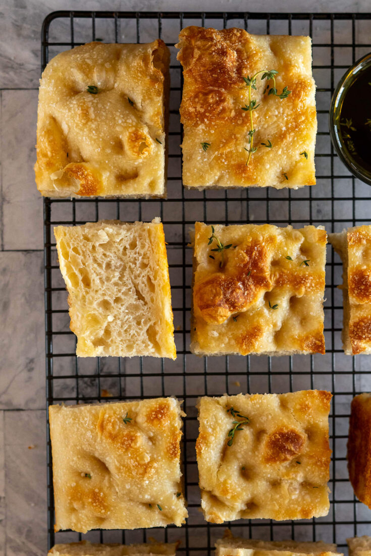 Sliced sourdough focaccia on a wire mesh rack with balsamic oil for dipping.