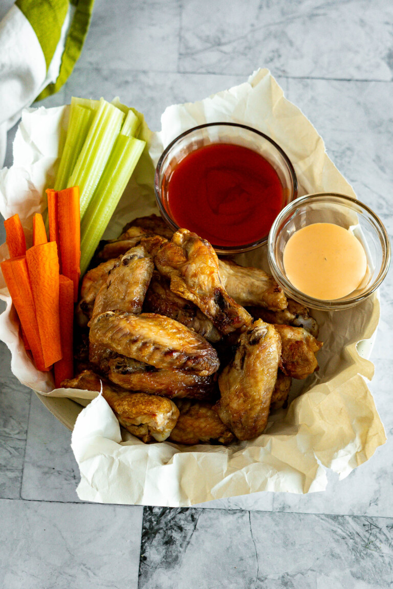 Frozen air fryer chicken wings in a bowl with hot sauce and celery sticks.