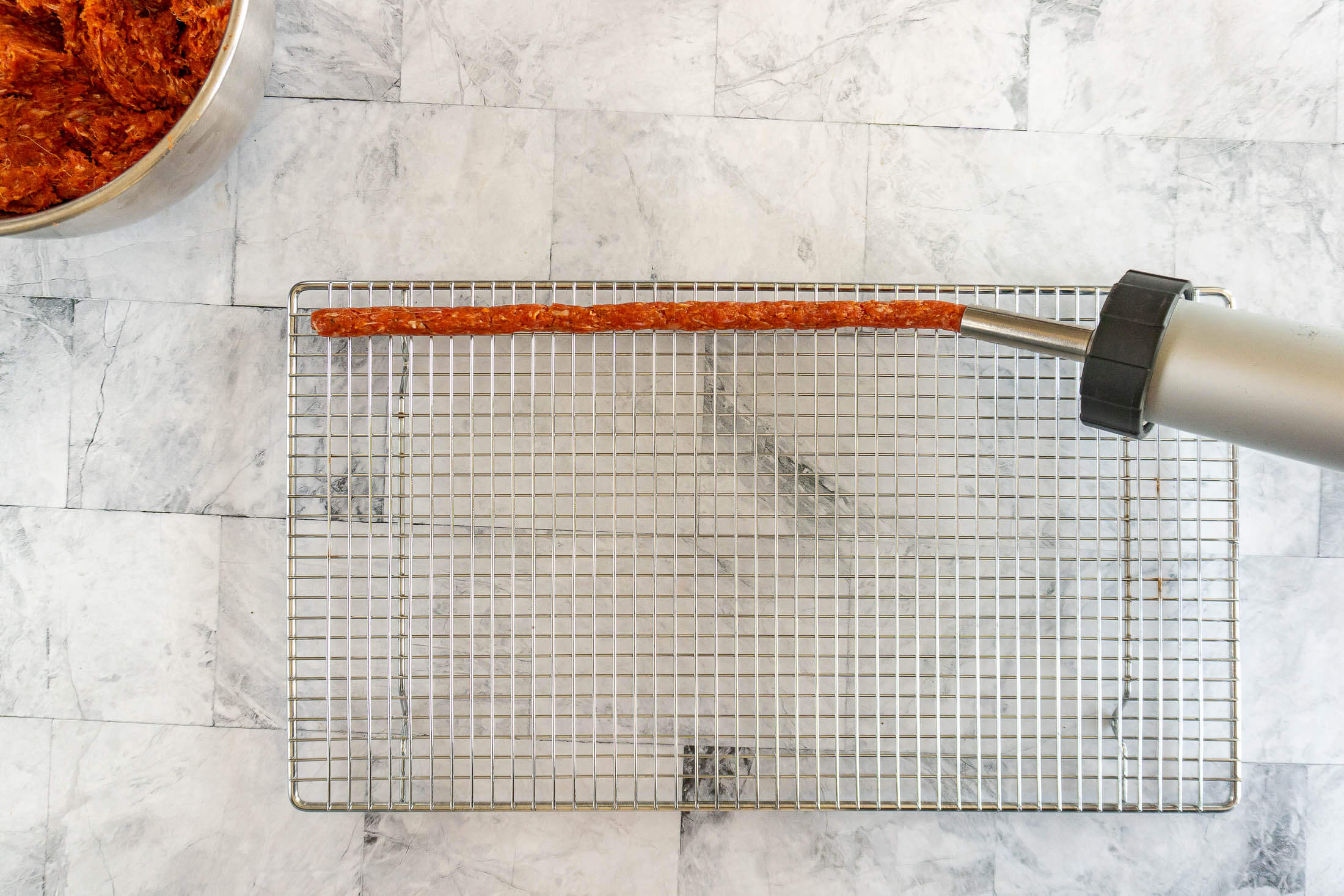 Piping out tubes of ground beef jerky onto a wire mesh rack.