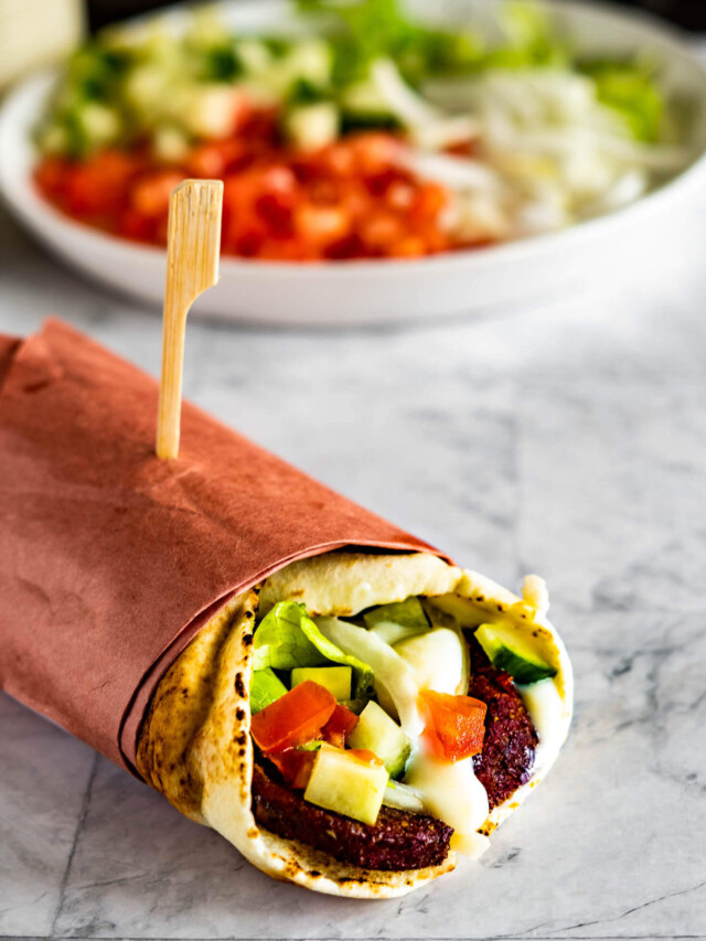A wrapped donair in front of a plate of chopped veggies.