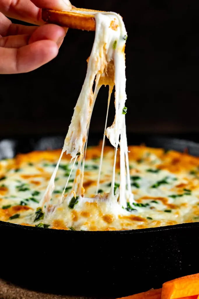 Taking a scoop of pulled pork dip, the mozzarella cheese is creating strings.