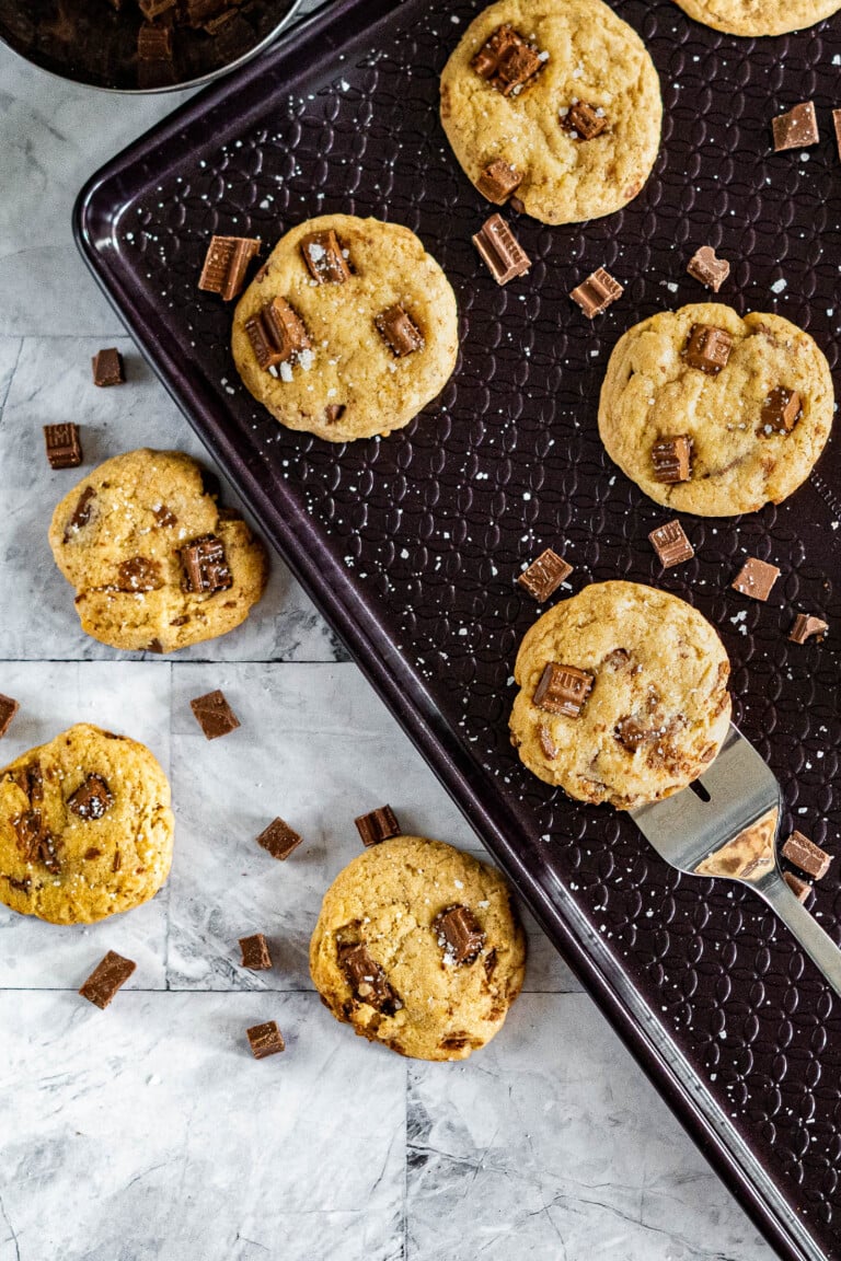 Scooping sourdough chocolate chip cookies off a baking sheet.