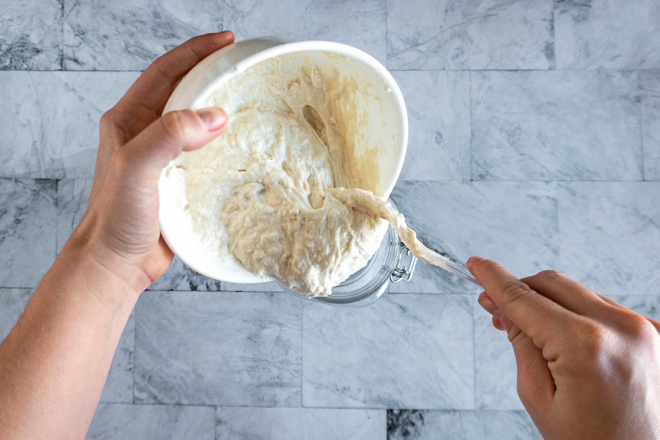 Pouring the fed sourdough starter into a clean jar.