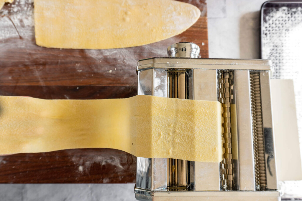 Long strip of sourdough pasta dough in the cutter of a pasta maker.