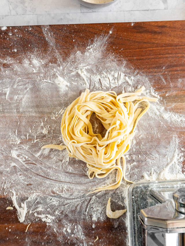 A nest of sourdough pasta on a floured cutting board.