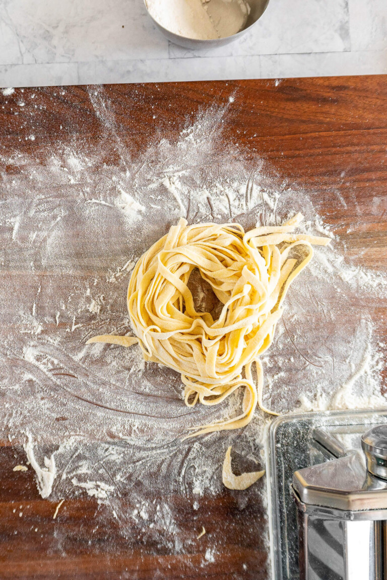 A nest of sourdough pasta on a floured cutting board.
